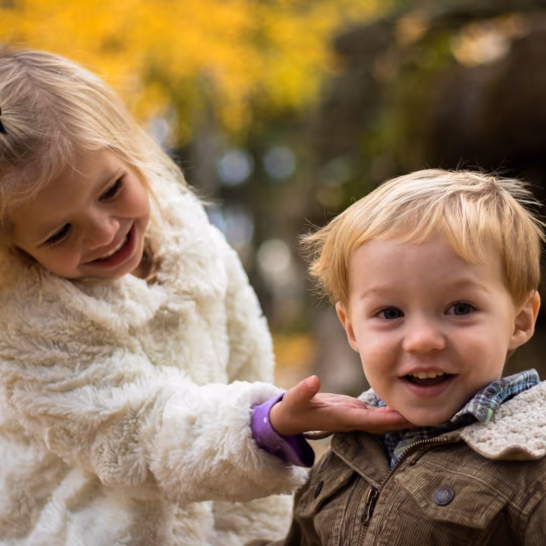 a little girl holding onto the chin of a younger boy