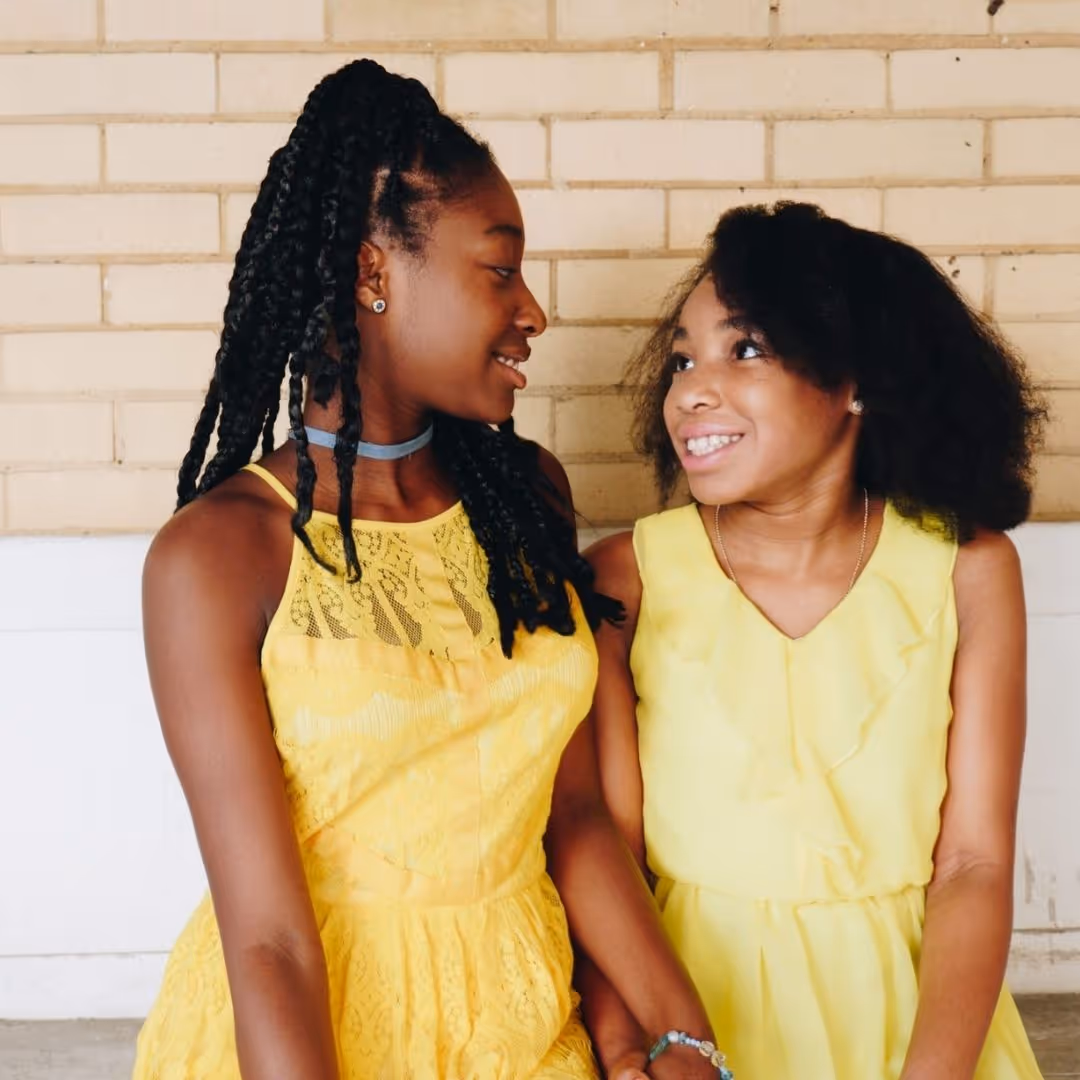 two sisters in bright yellow dresses smiling, looking at each other
