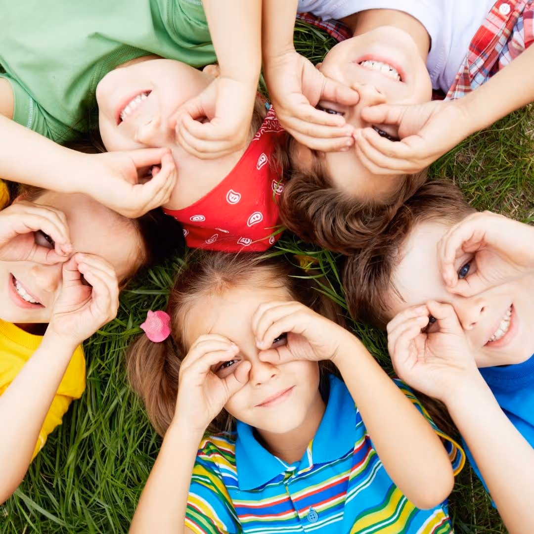 Kids looking up at a camera while lying on grass
