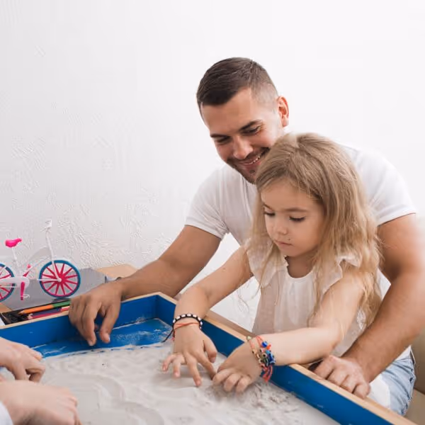 a father helps his daughter write in the sand