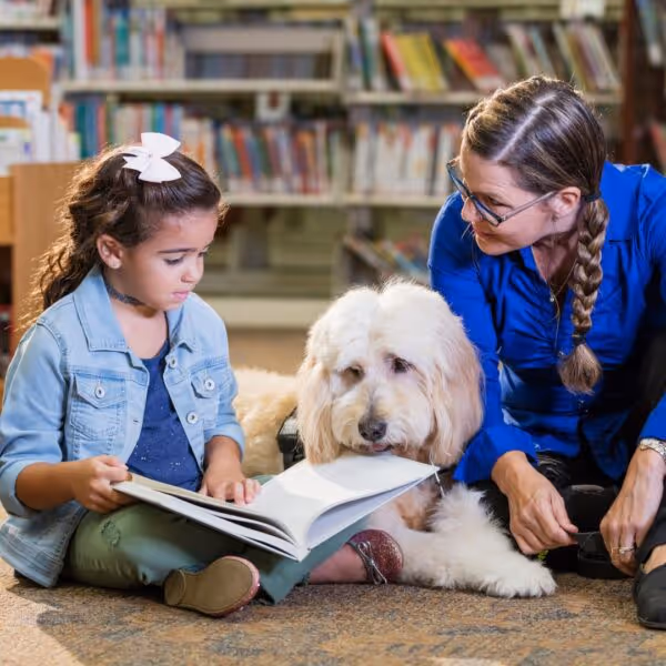 little girl reads a book with a white dog and therapist