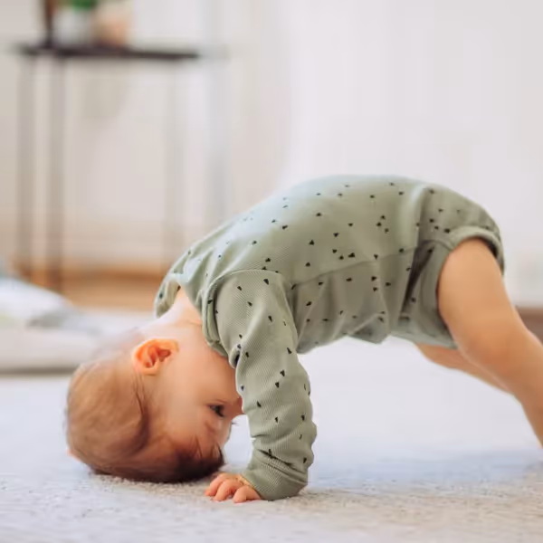 a baby on all fours with the crown of their head on the ground