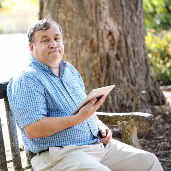 an adult with autism sitting on a bench holding a tablet