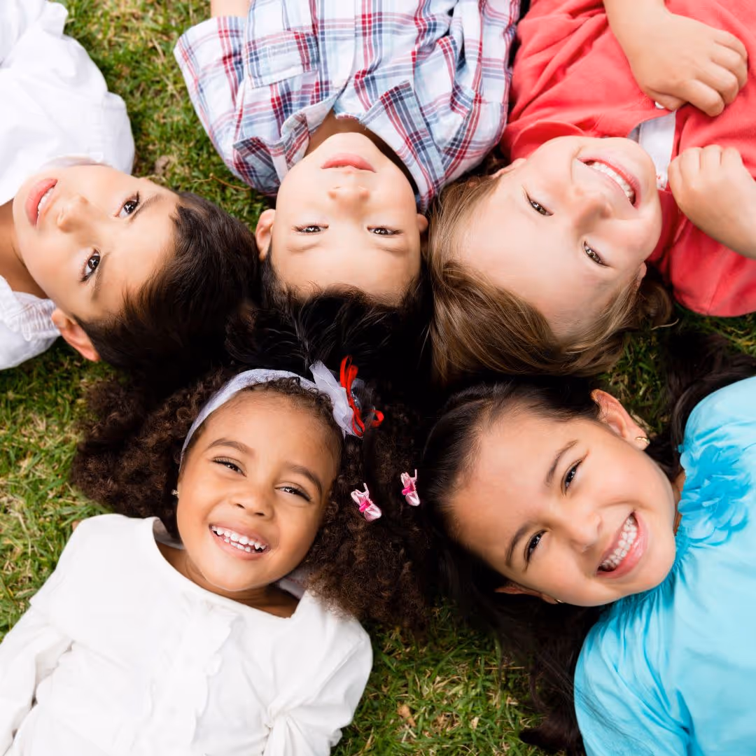 a group of kids laying in the grass smiling