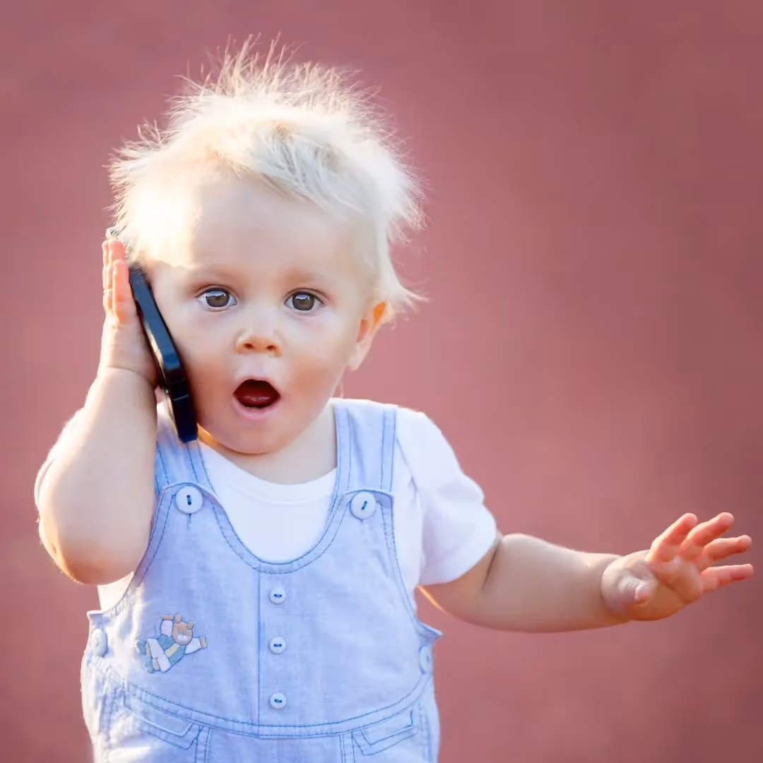 Young boy holding a phone up to his ear with his mouth wide open. 