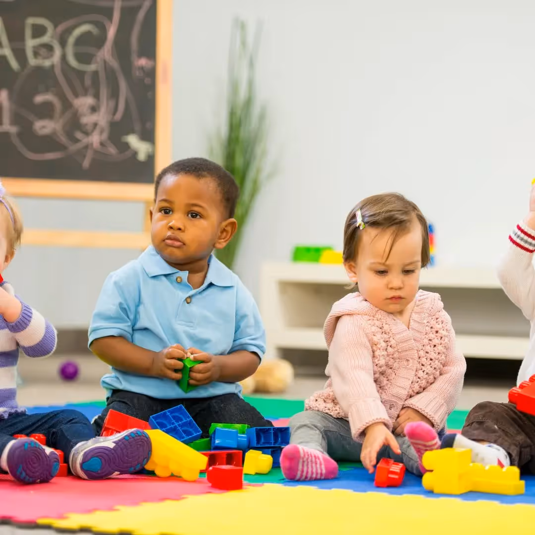 Two young kids sitting next to each other, playing with blocks. 