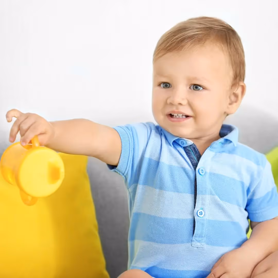 Young boy holding out a sippy cup with one hand.