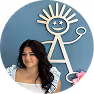 Smiling woman with long dark hair wearing a white top sitting in front of a blue wall with a large abstract white line drawing of a figure and a pink flamingo decoration.