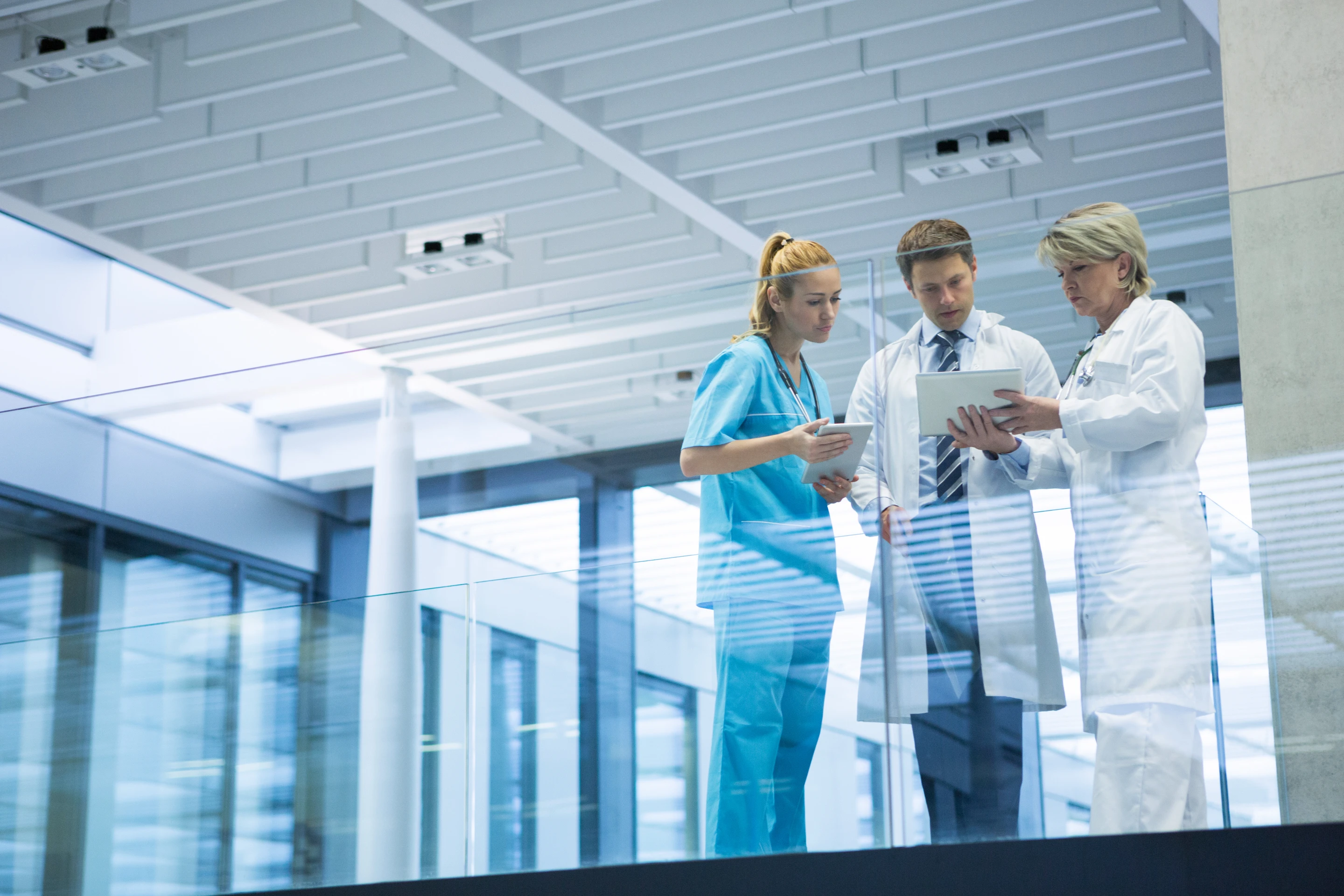 Medical team reviewing clinical data on tablet in hospital corridor