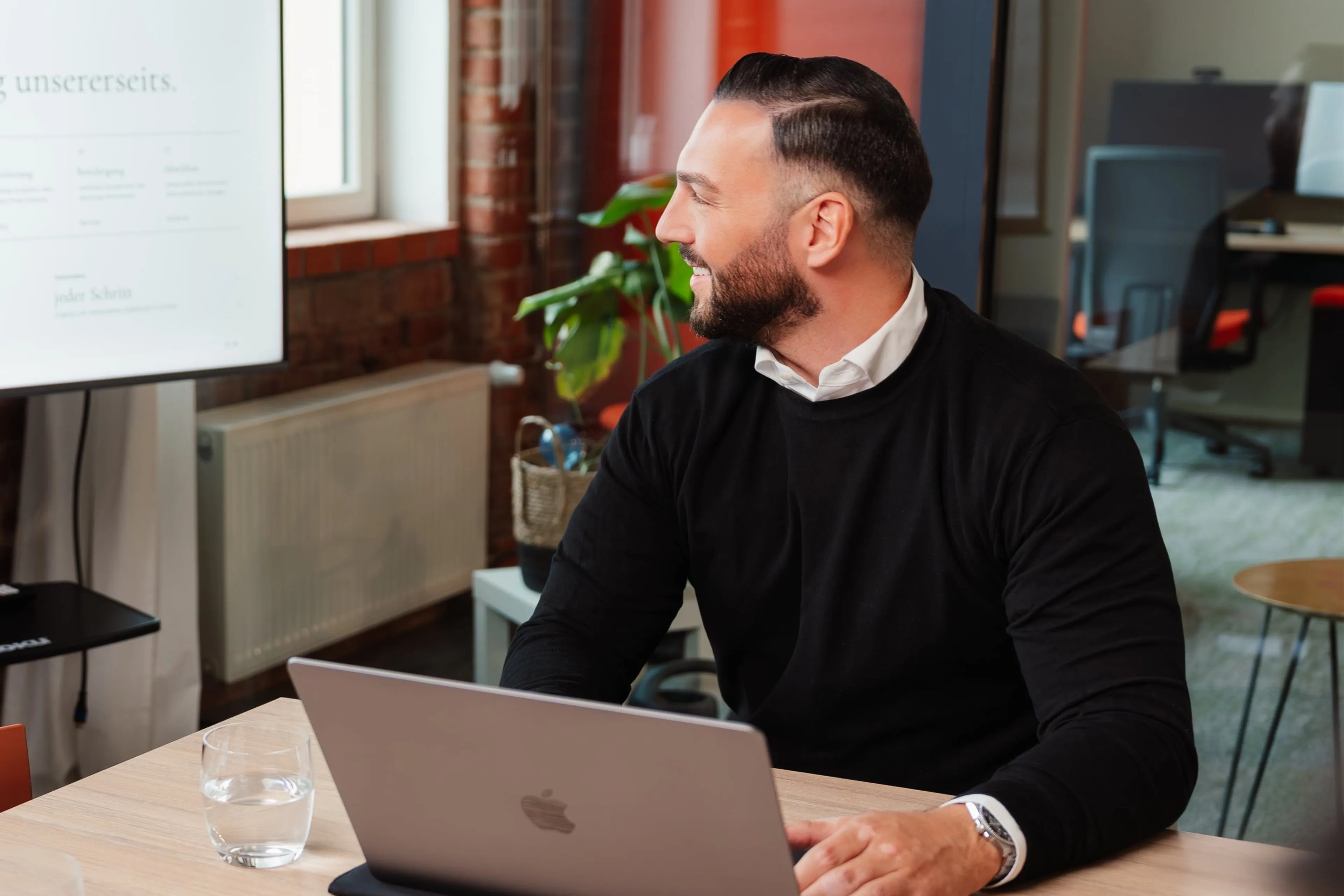 Berater am Laptop blickt auf eine Präsentation im Büro mit Backsteinwand