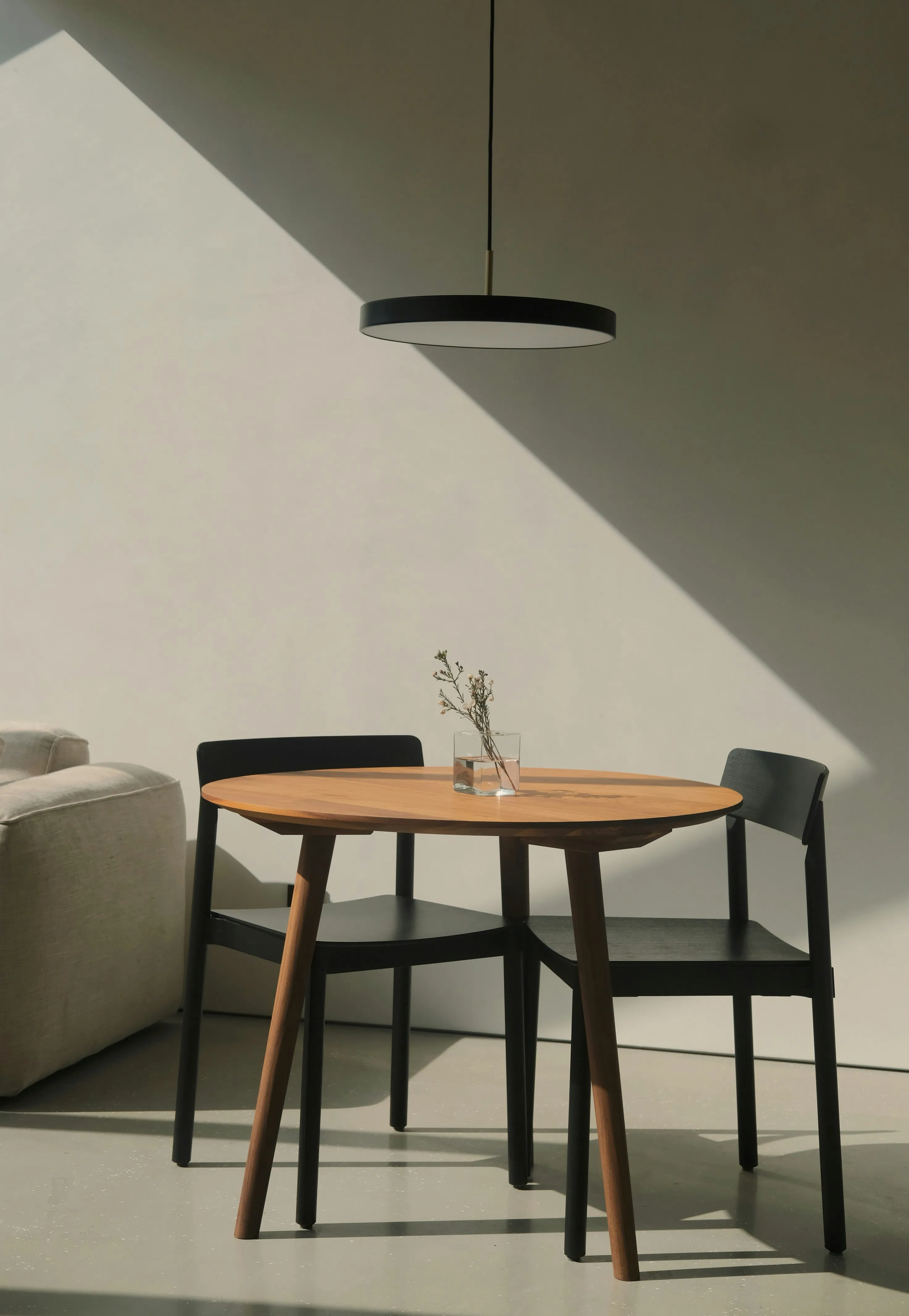 Minimalistisch eingerichtete Essecke mit rundem Holztisch, zwei Stühlen und Pendelleuchte
