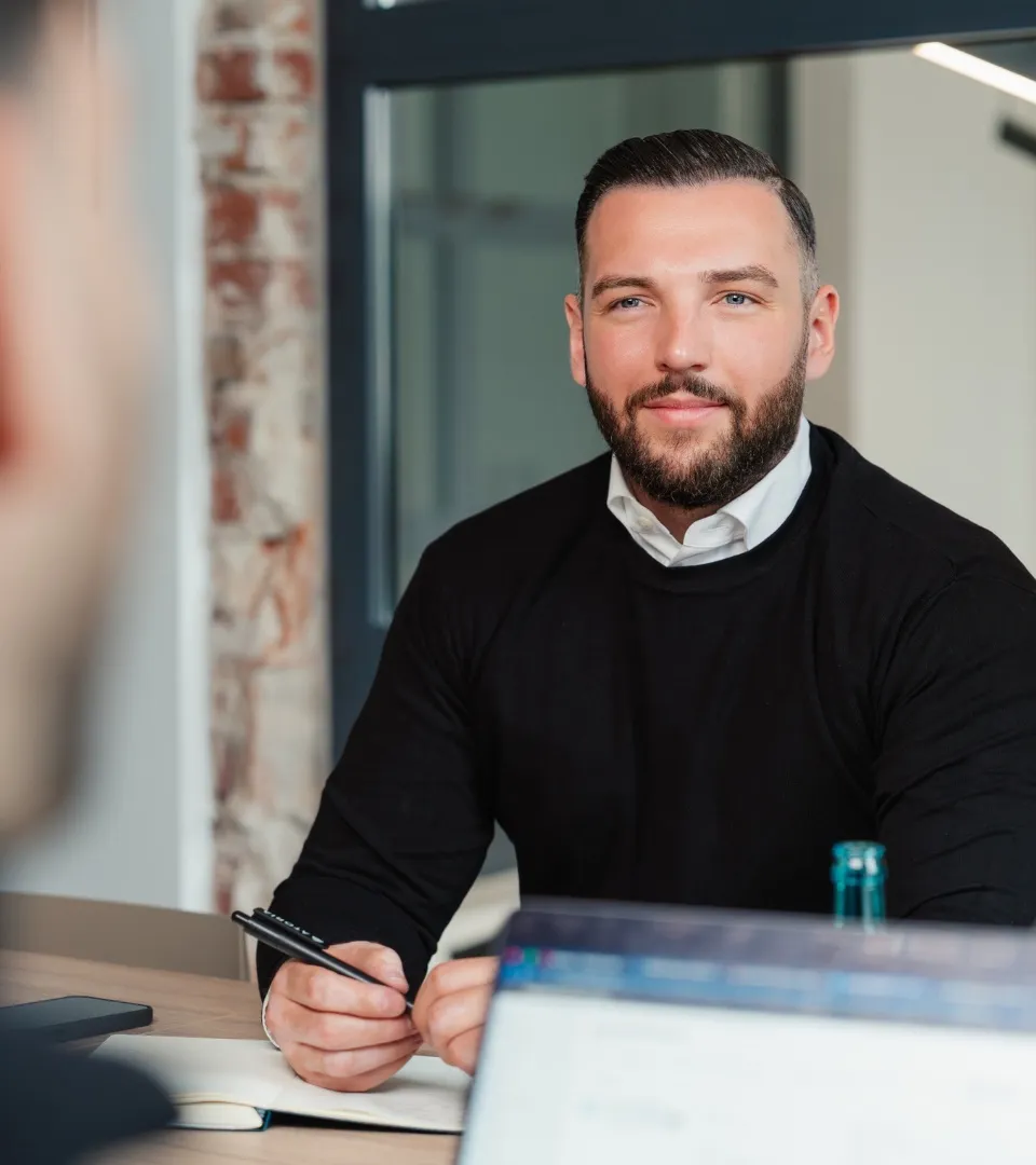 Immobilienberater mit Stift und Notizblock am Tisch während eines Beratungsgesprächs