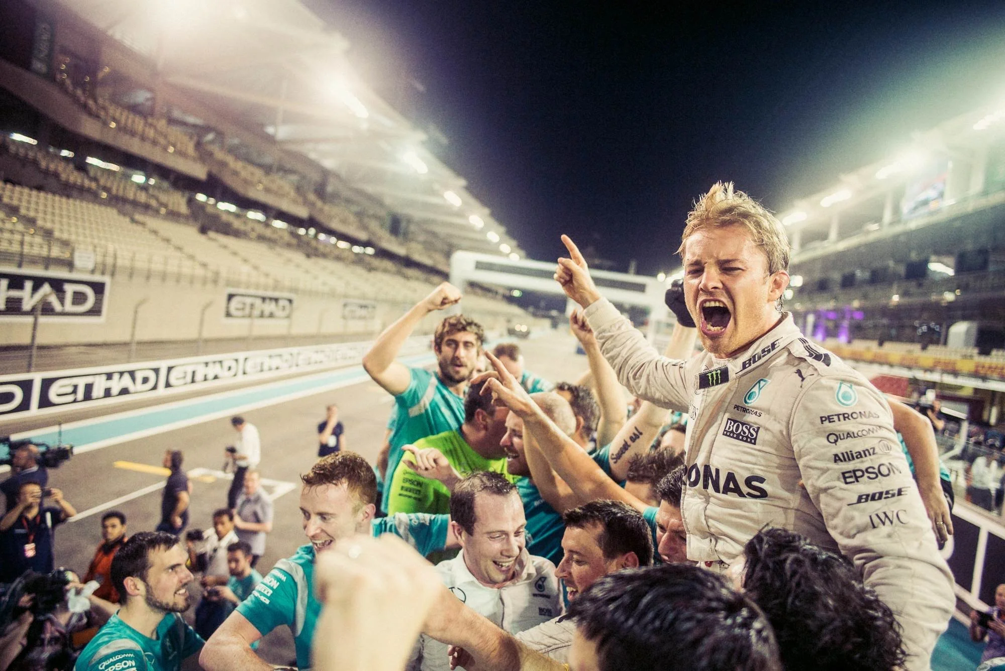 Excited Mercedes-AMG Petronas Formula 1 driver celebrating with team members on the race track at night.