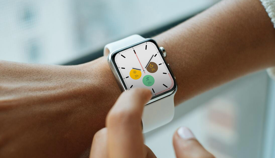 Person interacting with a white smartwatch displaying a clock face with three colored circular icons showing activity durations.