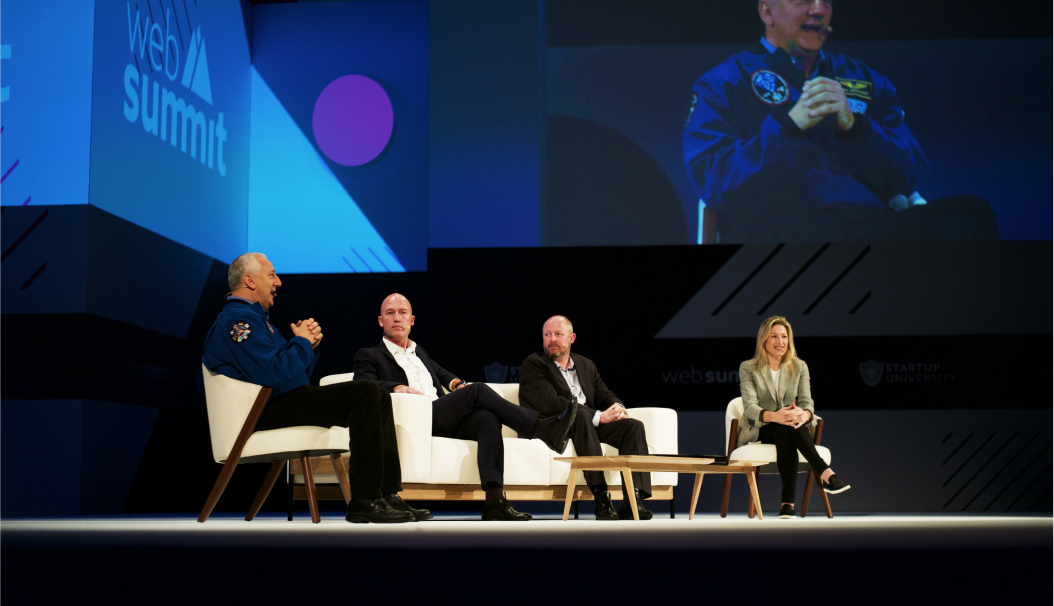 Four people seated on stage during a Web Summit panel discussion with a large screen behind them.