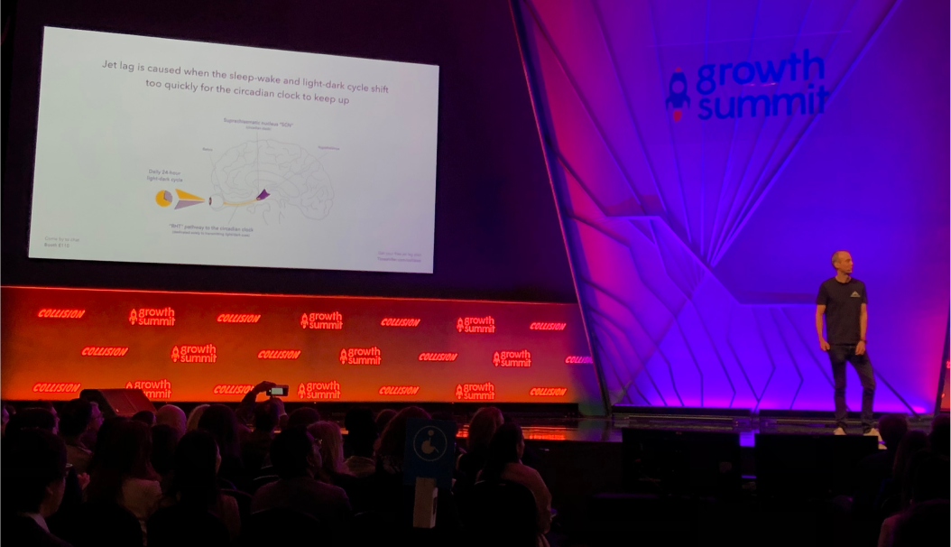 Speaker presenting on jet lag and circadian rhythm at Growth Summit with audience and projected slide showing brain diagram and sleep-wake cycle explanation.