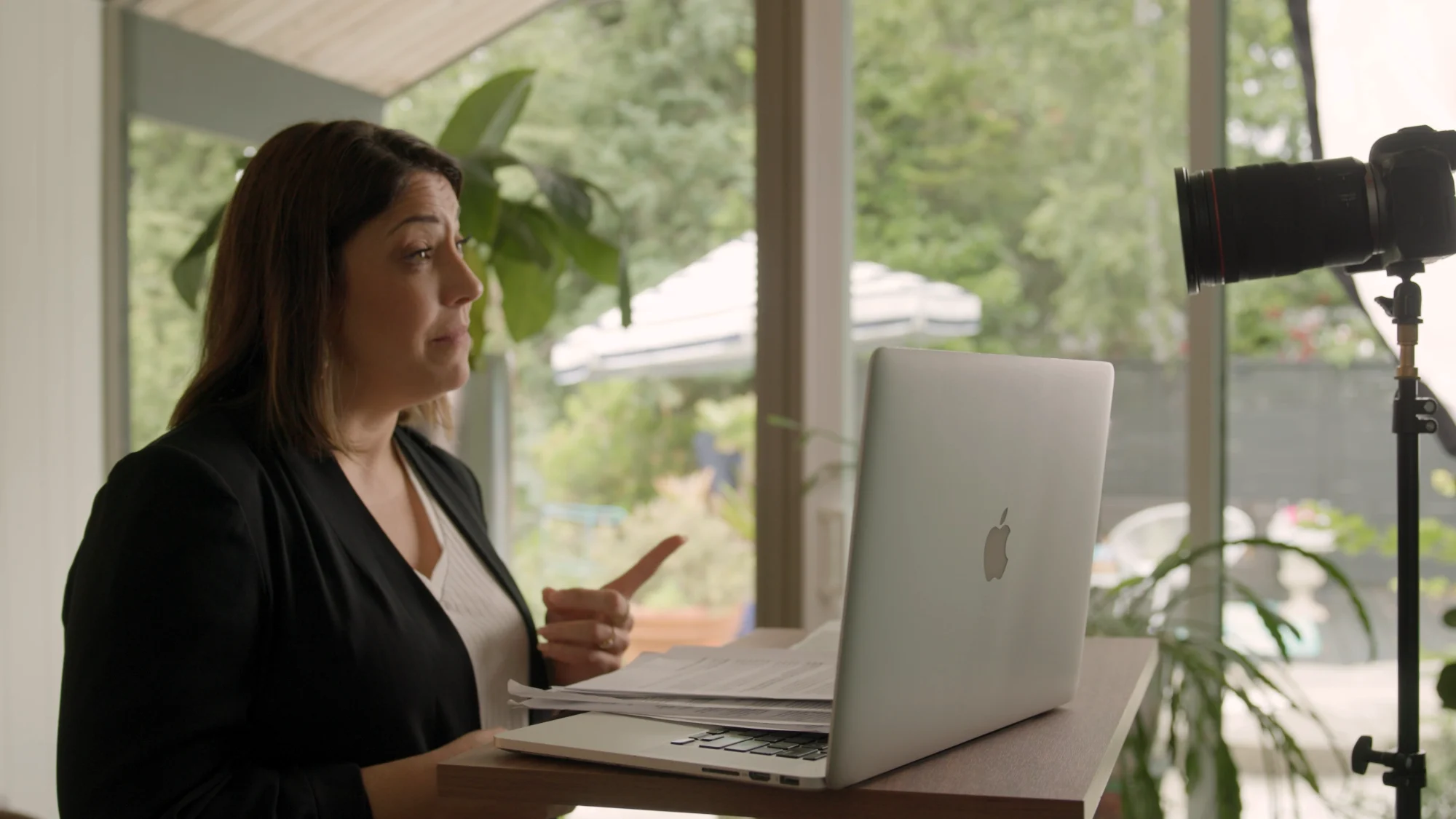 Elena sitting at a desk, working on a laptop and speaking to camera at the same time.