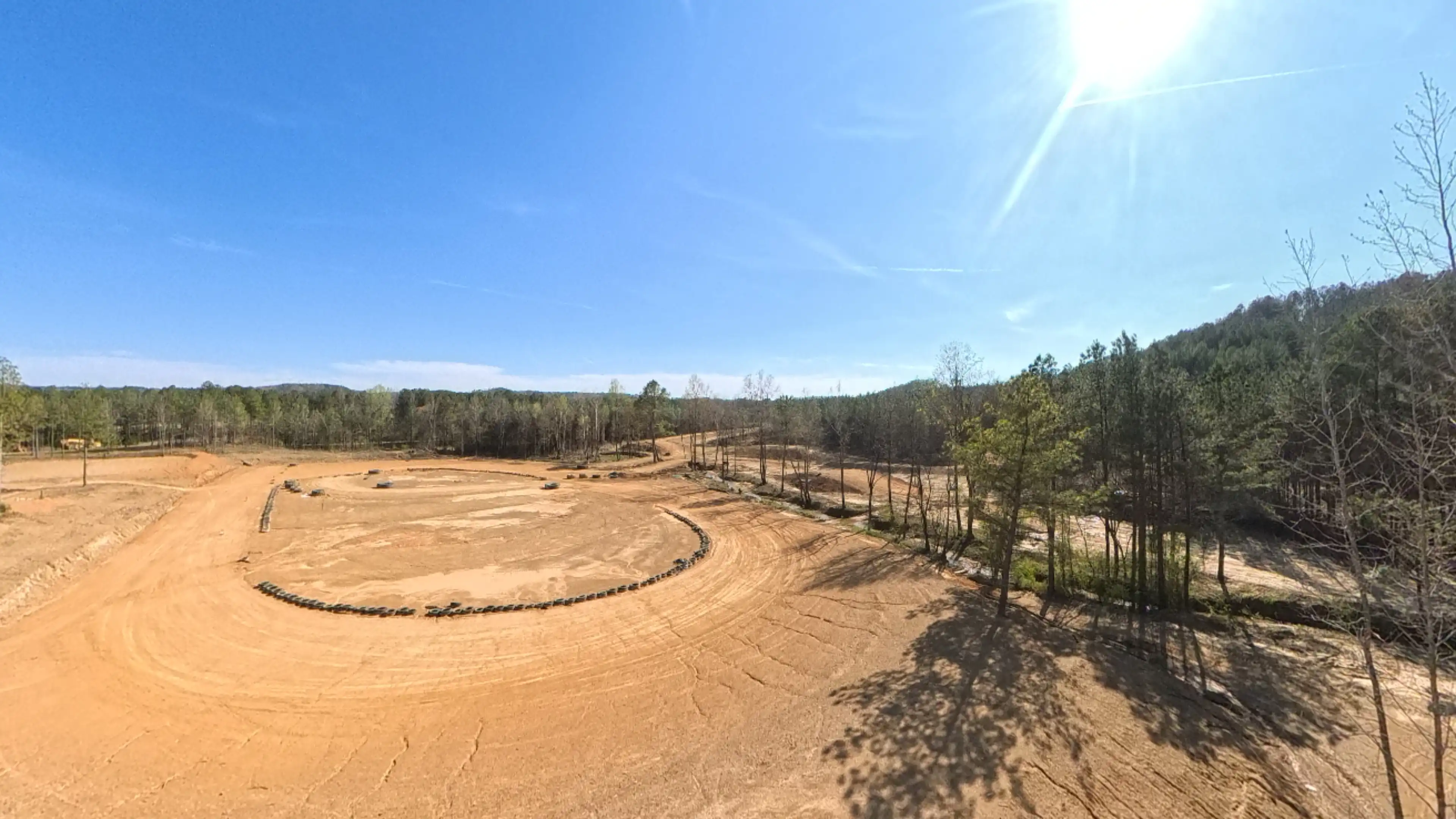 Wide view of a dirt motocross track surrounded by trees under a bright sunny sky.