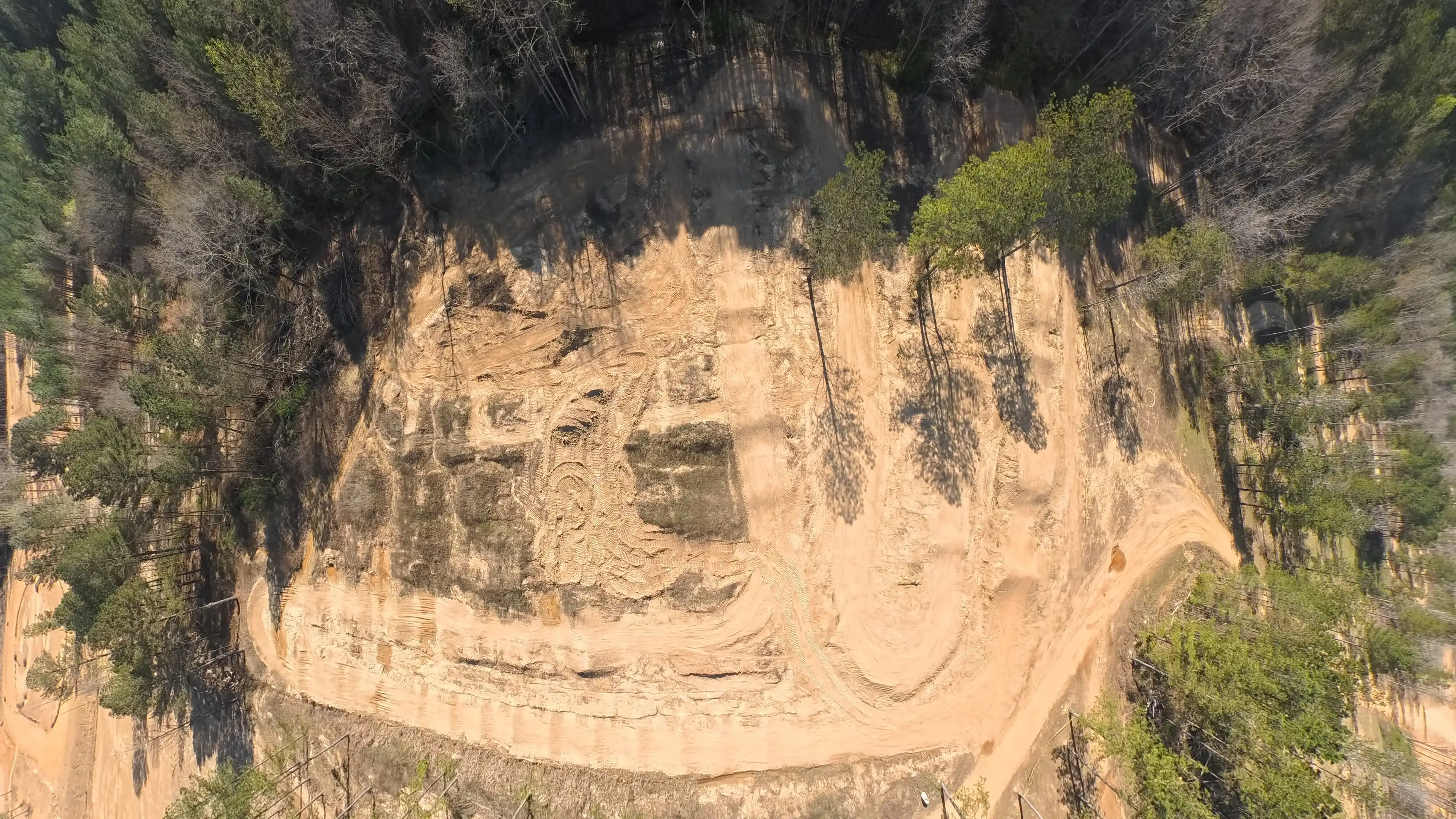 A cleared dirt track surrounded by dense trees, viewed from above in a forested area.