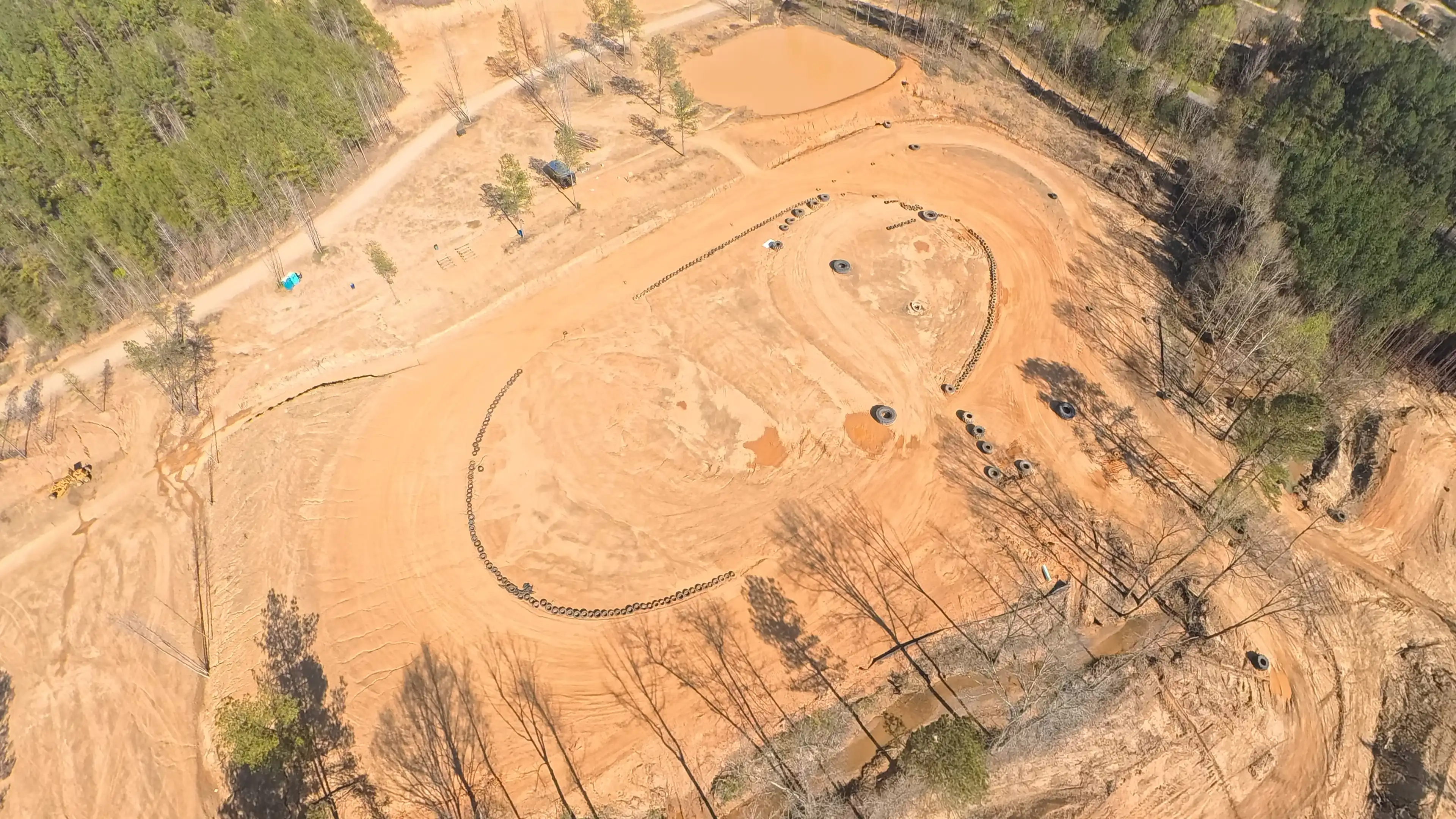 Aerial view of a dirt motocross track surrounded by trees and marked with tires.