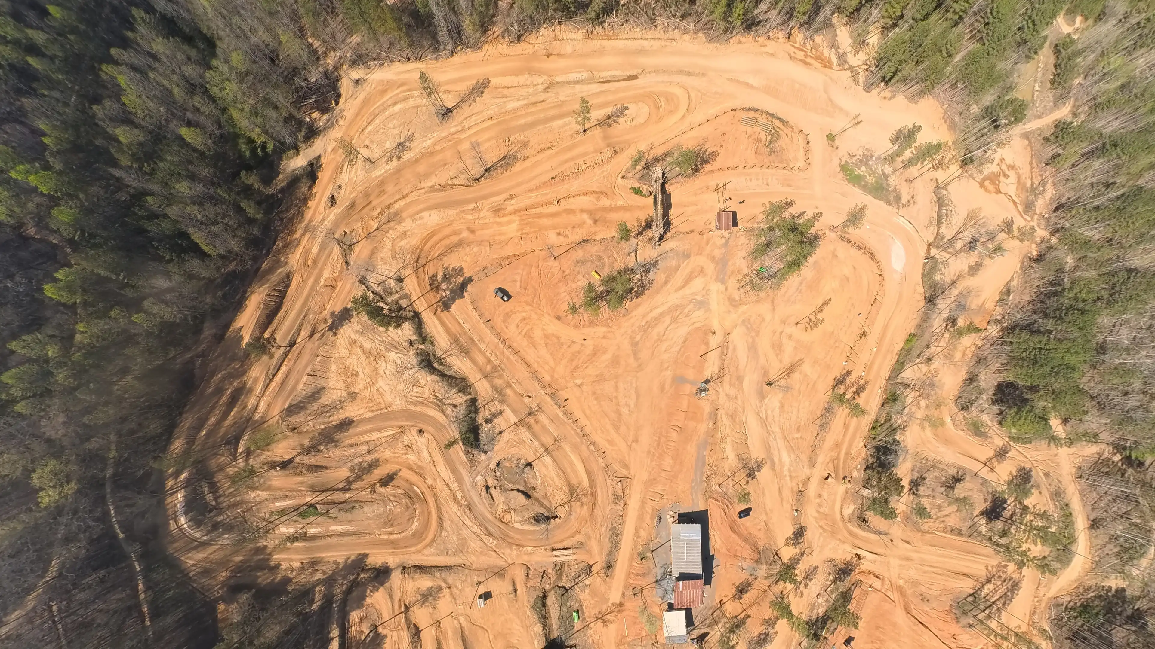 Overhead view of a dirt motocross track surrounded by trees with winding paths and a few scattered structures.
