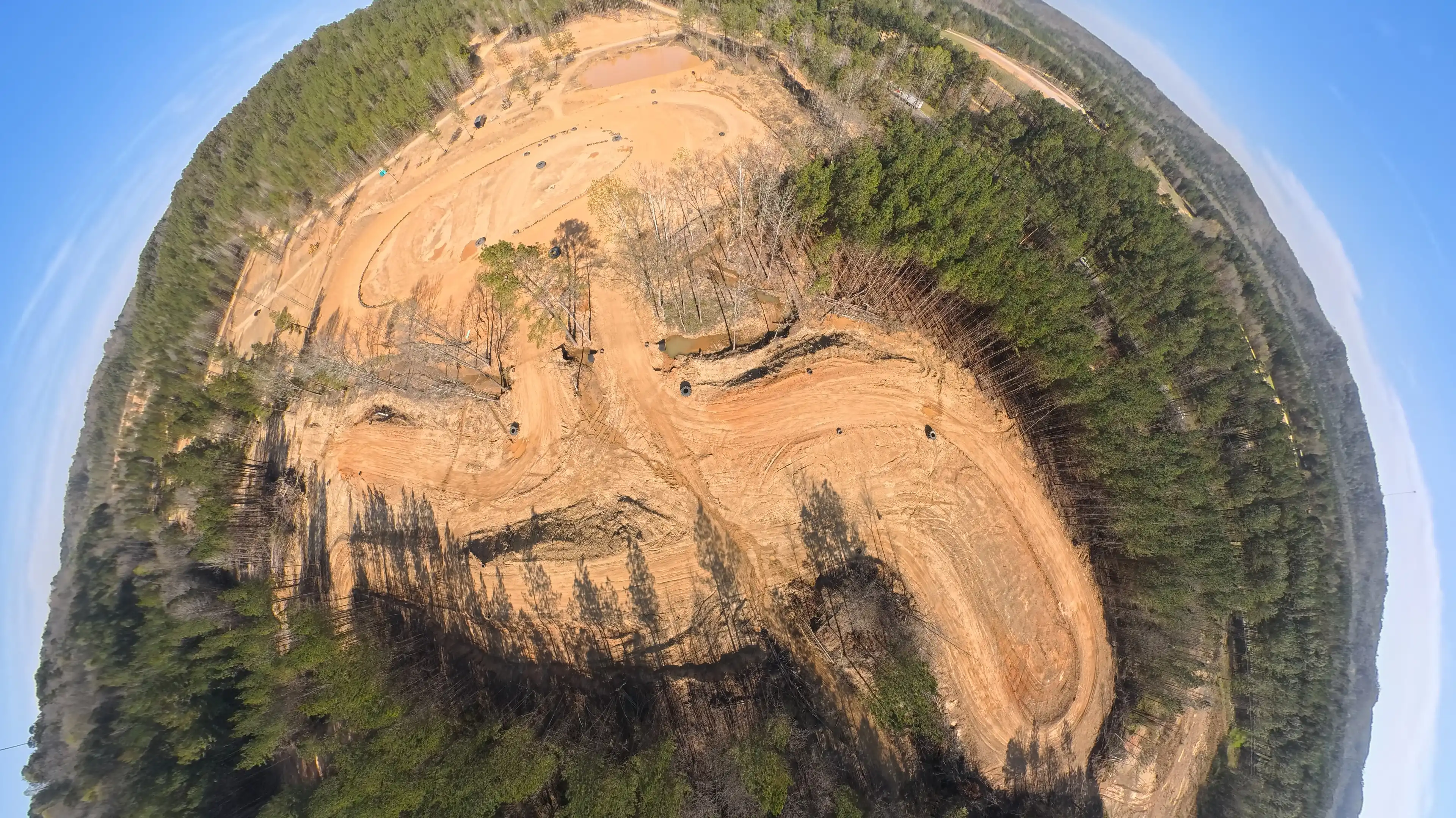 Aerial view of an off-road dirt track surrounded by dense forest with clear blue sky.