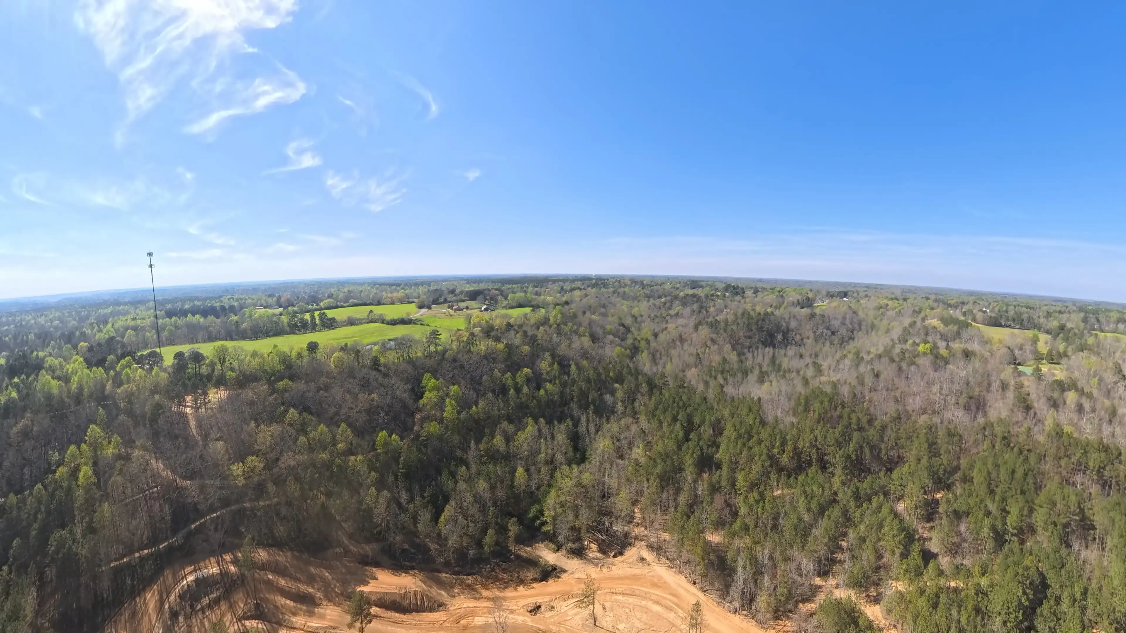 Aerial view of a forested landscape with patches of green fields under a clear blue sky.