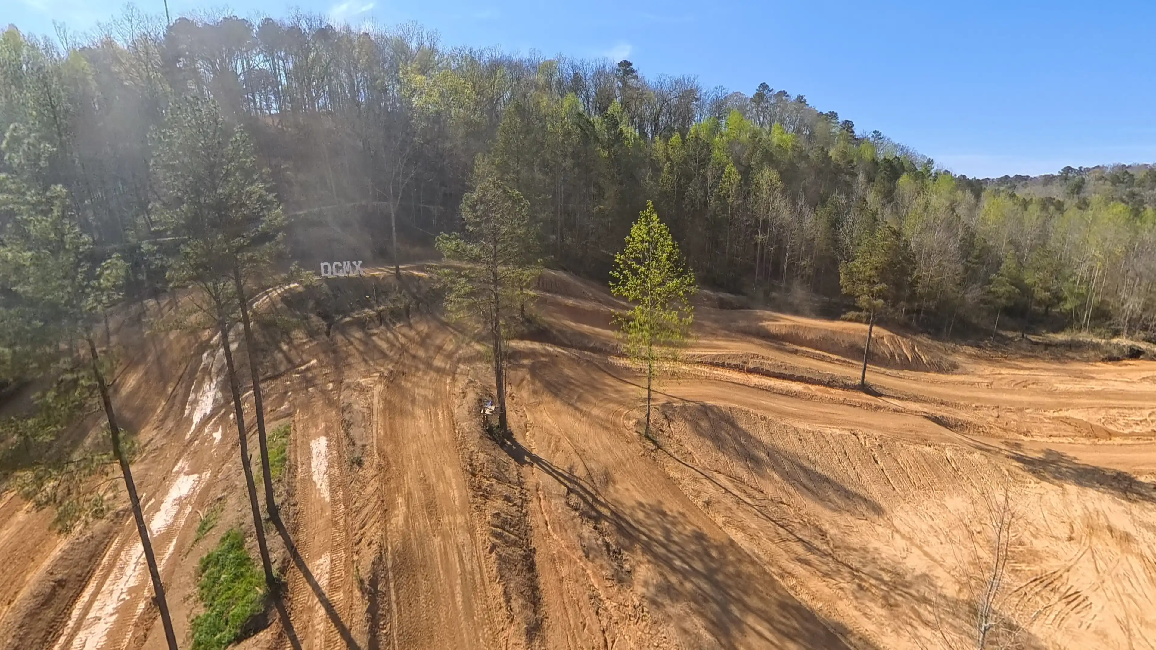 A dirt motocross track with multiple rough trails surrounded by trees under a clear blue sky.