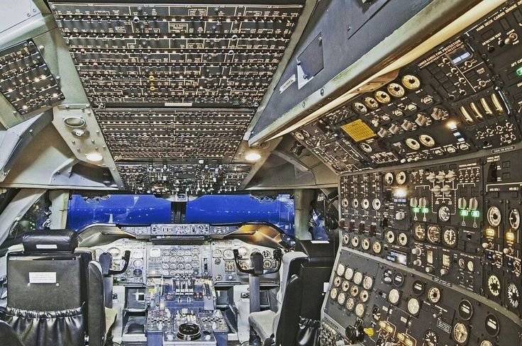 Cockpit of an aircraft showing multiple control panels, instruments, switches, and two pilot seats.