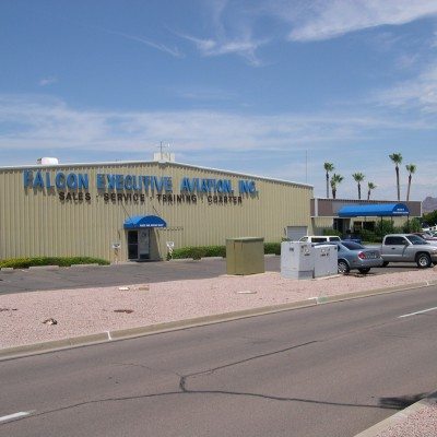 Falcon Executive Aviation, Inc. building with blue awnings and cars parked outside on a sunny day.