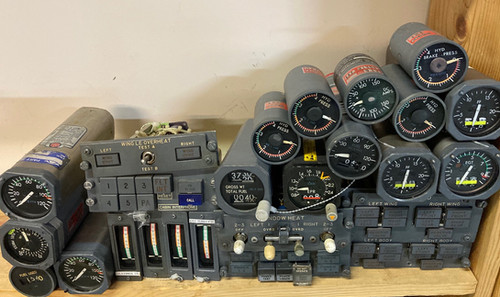 A collection of vintage aircraft cockpit instruments including gauges, dials, and switches arranged on a wooden shelf.