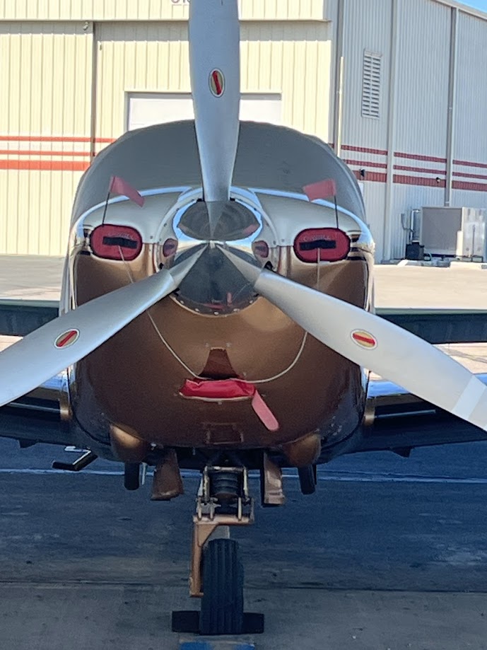Front view of a small single-engine propeller airplane parked in front of a hangar.