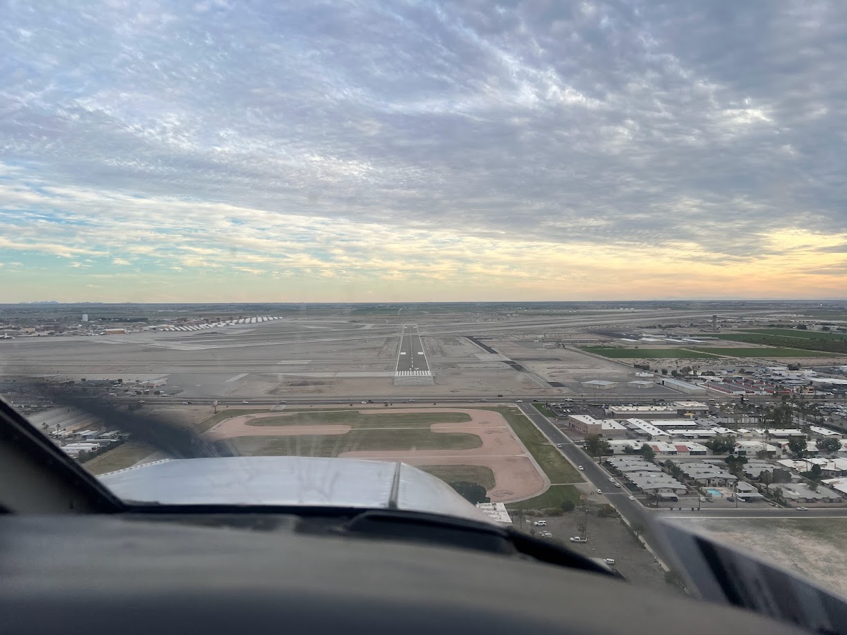 View from inside a small airplane approaching a runway for landing with a cloudy sky and urban landscape nearby.