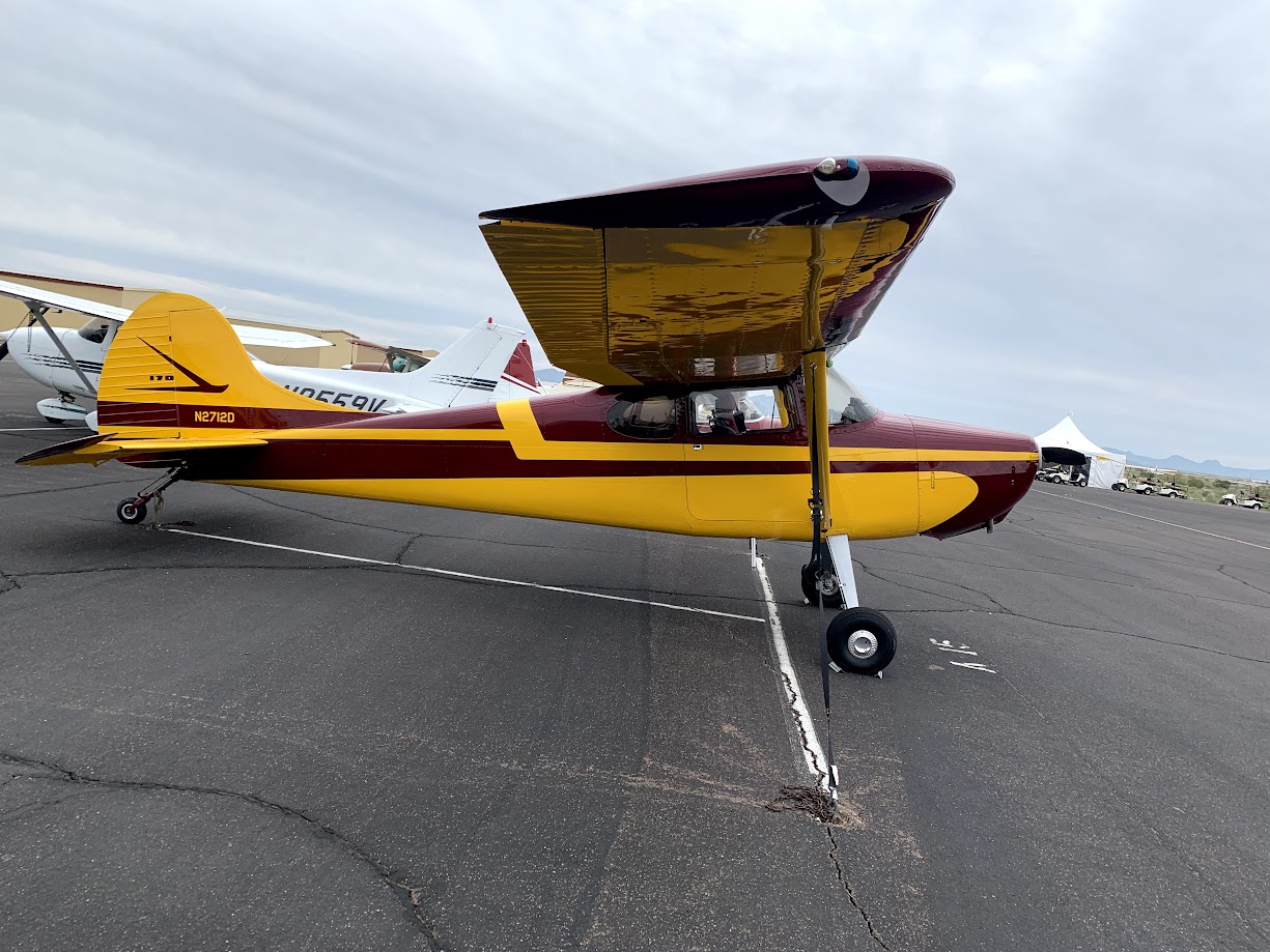 Maroon and yellow vintage single-engine airplane parked on an asphalt runway under a cloudy sky.