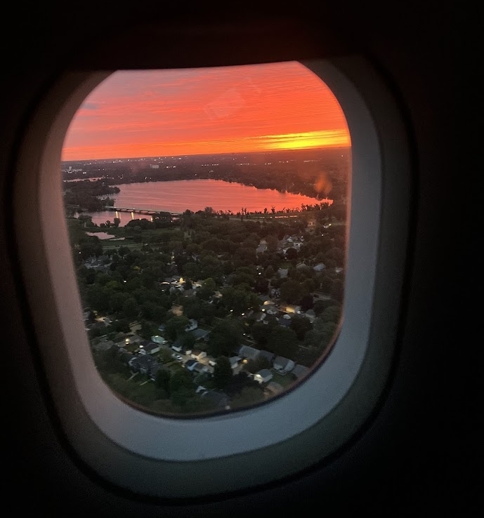 View of a lake, neighborhood, and a bright orange sunset sky seen through an airplane window.