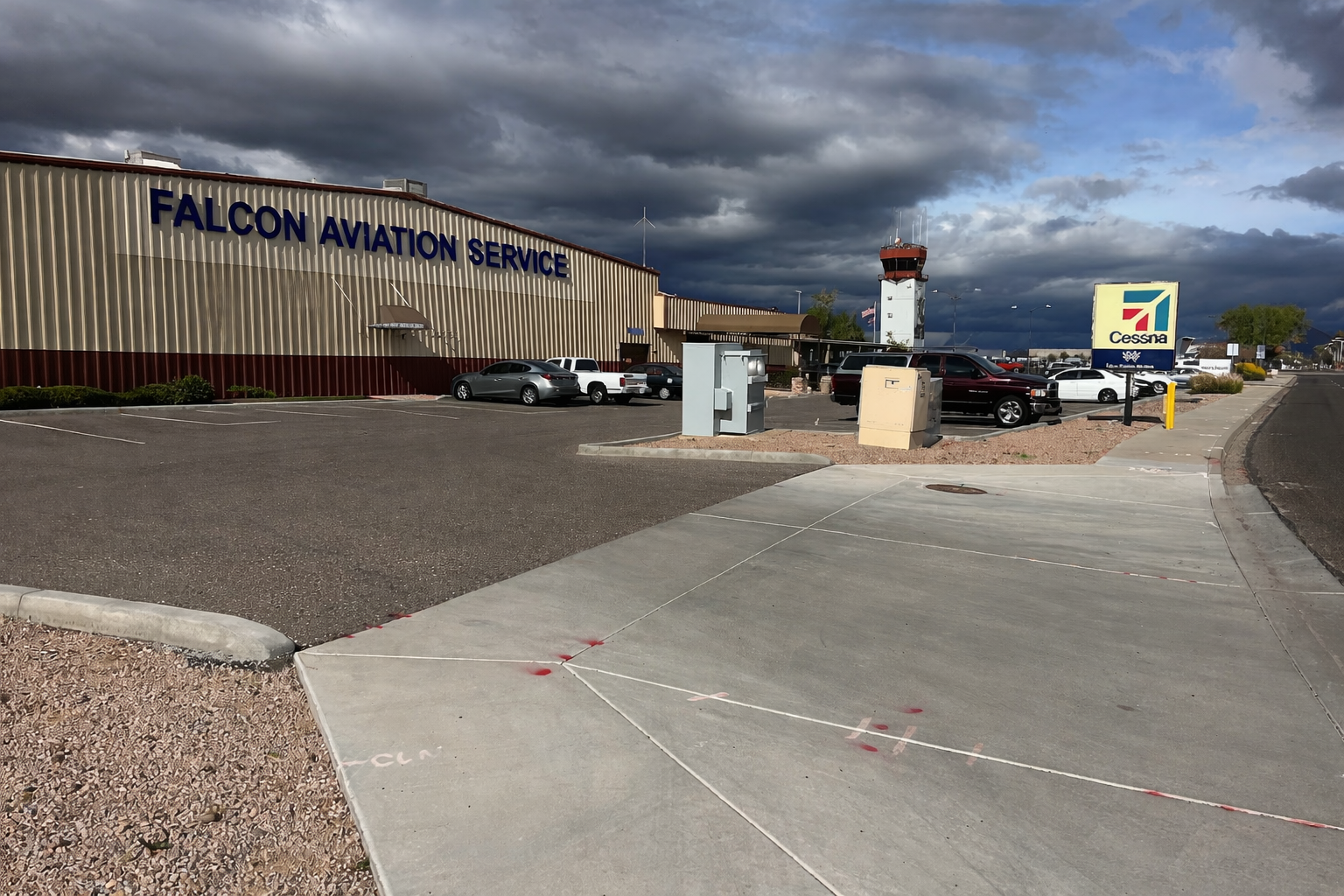 Outdoor view of Falcon Aviation Service building with parked cars and a Cessna sign under a cloudy sky.