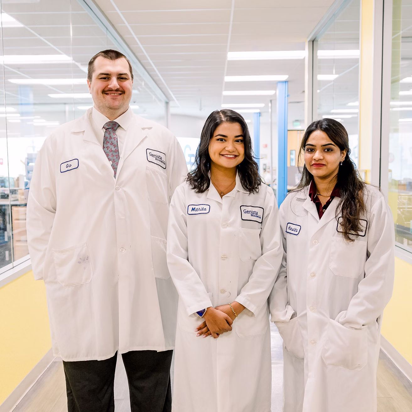 Three dental professionals wearing white lab coats smiling in modern dental office