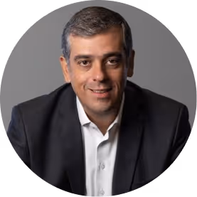 Homem de terno preto sorrindo com fundo cinza neutro.