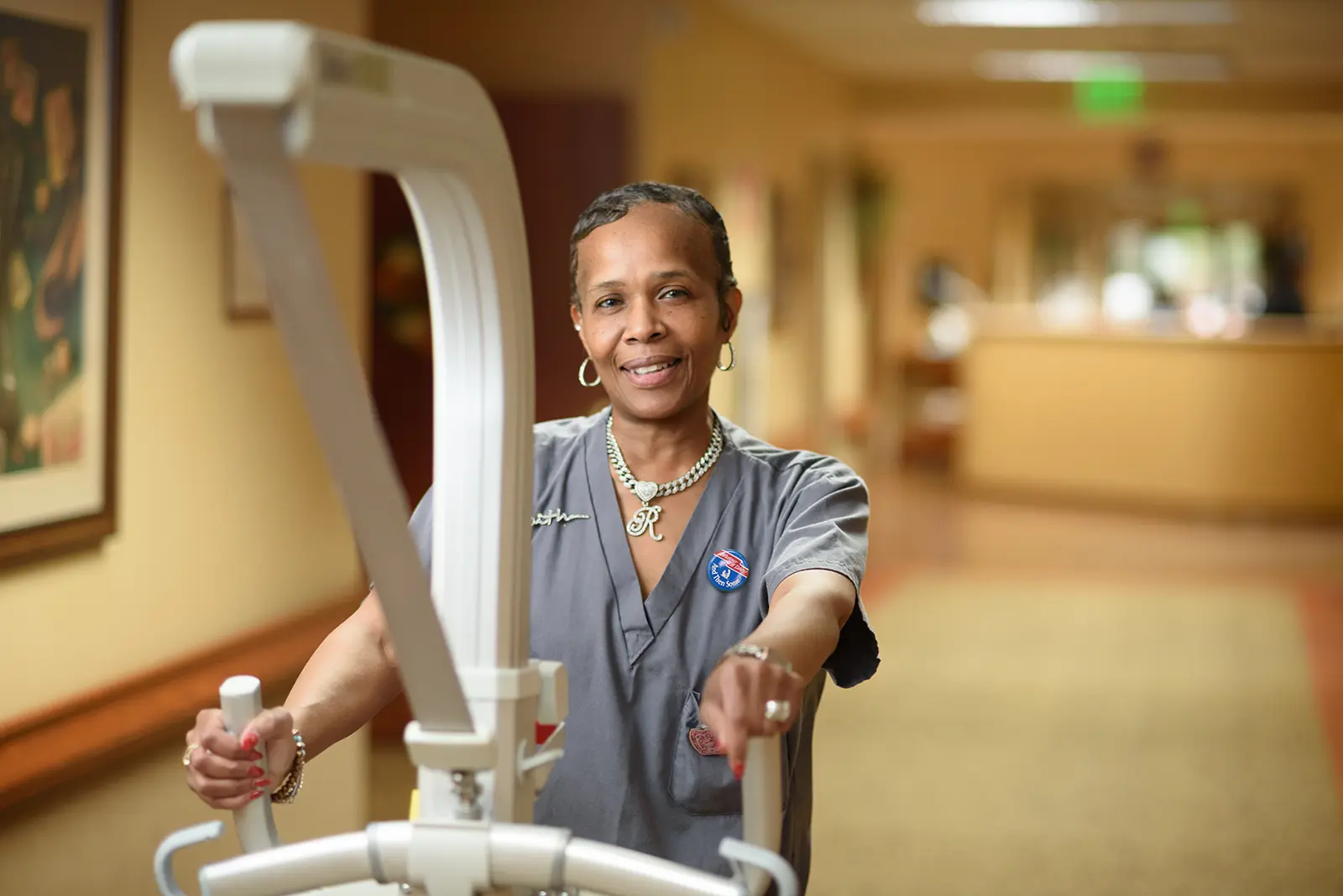 An Old Hickory Village associate smiles while guiding a patient lift down a hallway
