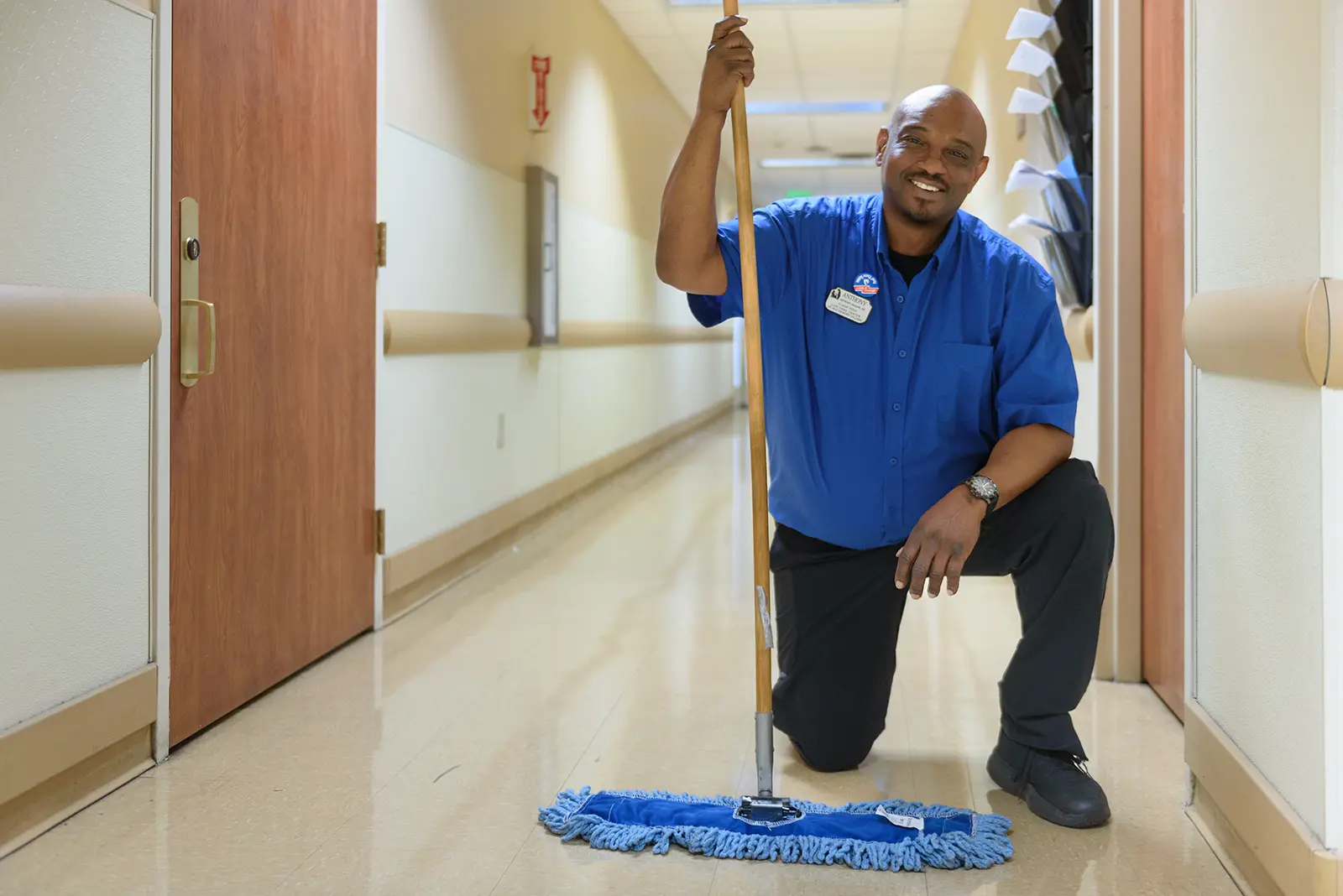 A housekeeping associate kneels with a mop in a hallway