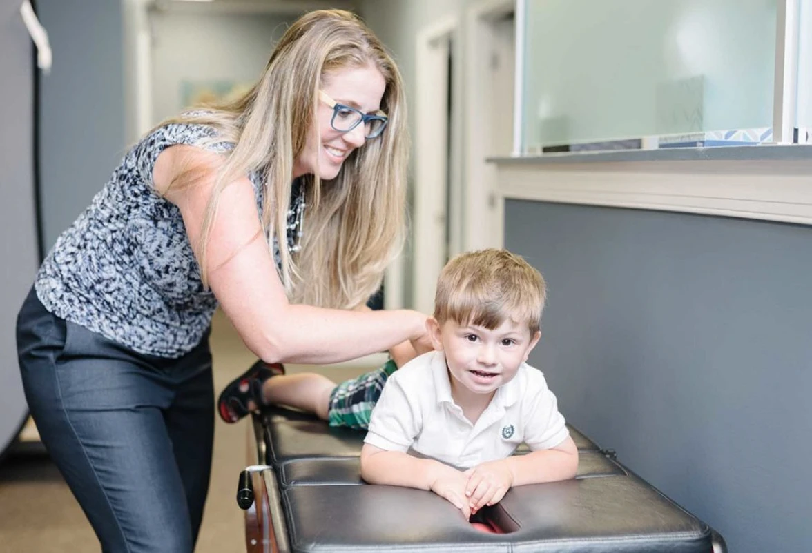 Smiling young woman adjusting a boy lying face down on a medical examination table in a clinic.