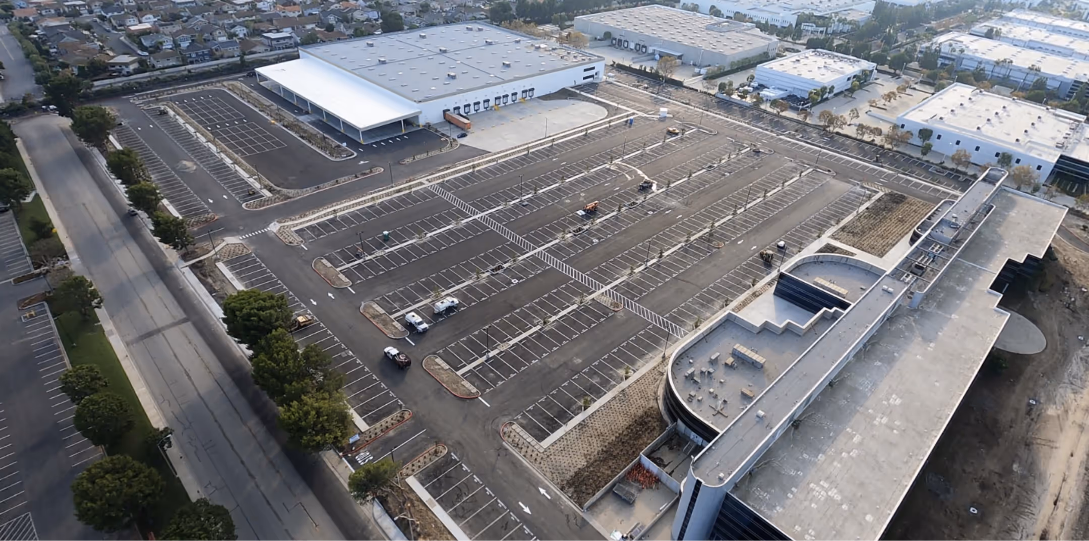 Aerial view of a large parking lot with mostly empty spaces surrounding industrial buildings.