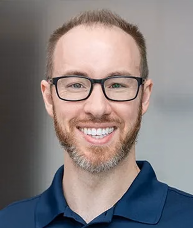 Smiling man with glasses, short hair, and a beard wearing a navy blue collared shirt.