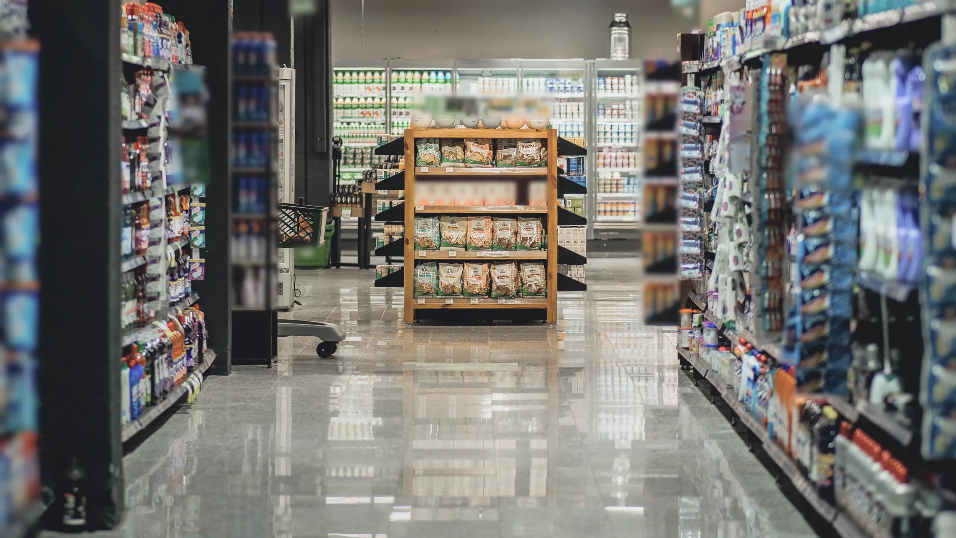 A wide grocery store aisle after closing, with stocked shelves on both sides and a wooden display in the center.