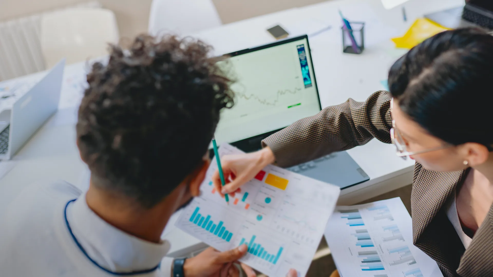 A founder and an advisor reviewing a line chart on a laptop and printed charts on a desk.