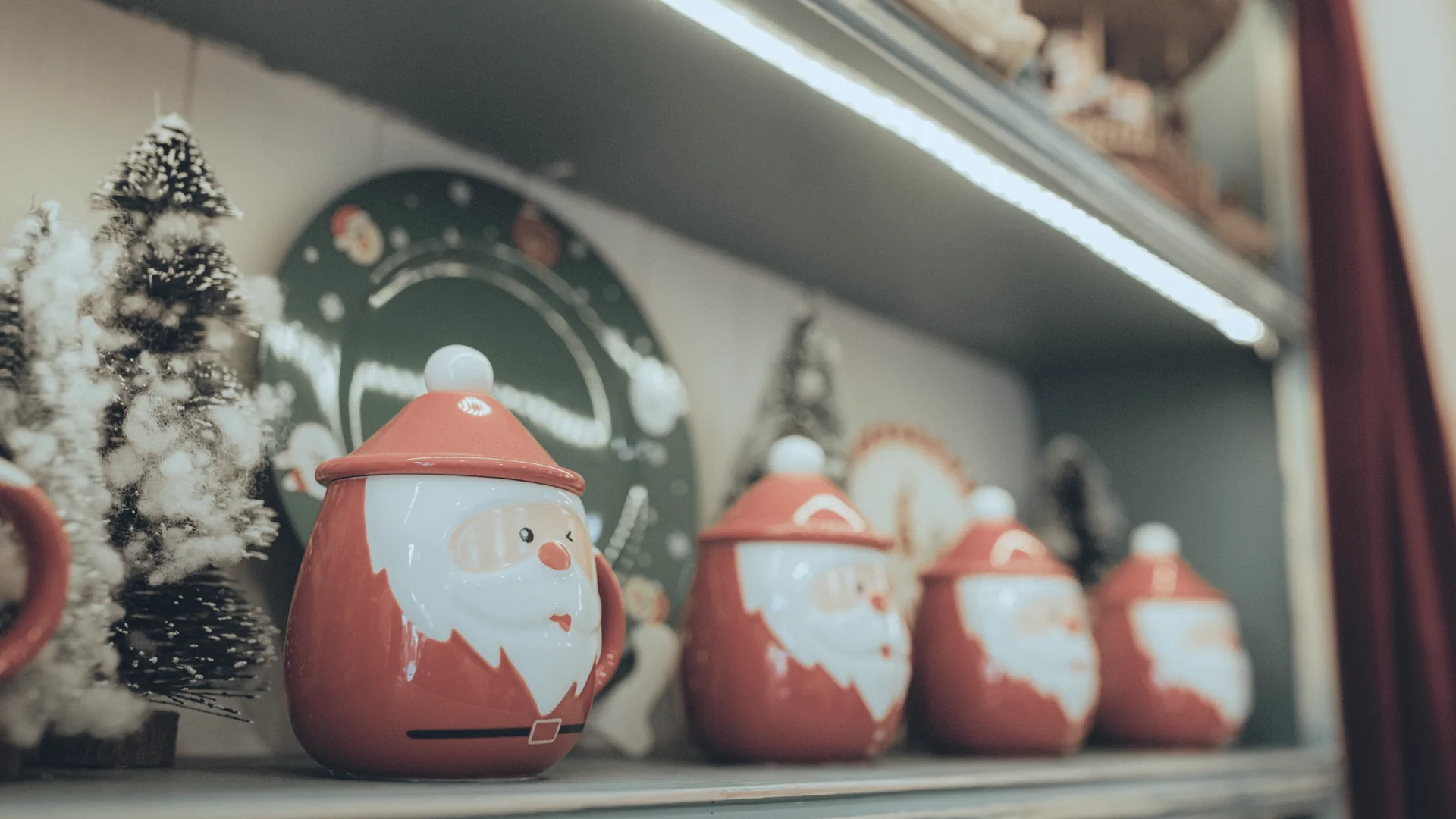 A holiday display shelf with Santa jars and frosted mini trees in a lit shop.
