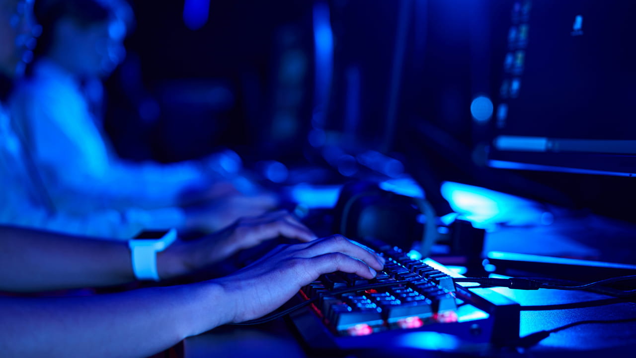 Individual engaged in typing on a keyboard, with a computer screen displaying content.
