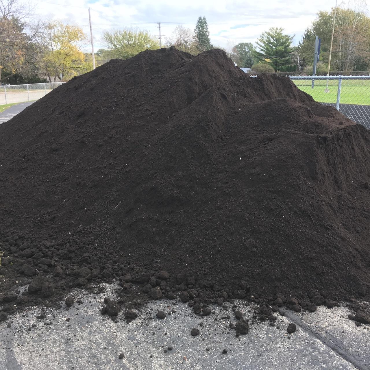 Large piles of dark rich compost on a paved surface showing the focus of the company.