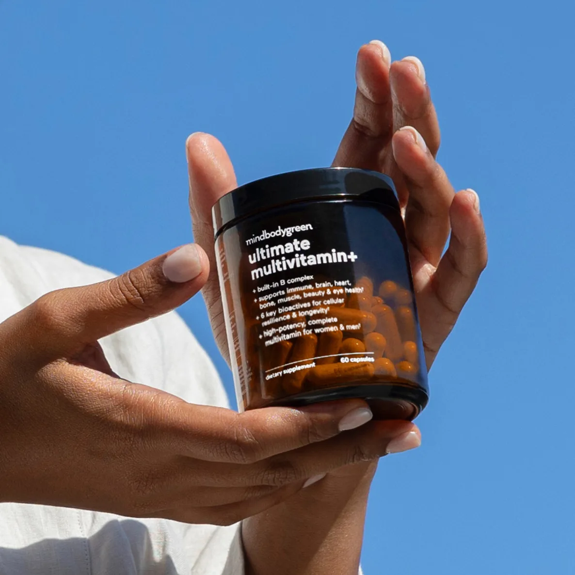 mindbodygreen ultimate multivitamin bottle held by model in hands with blue background
