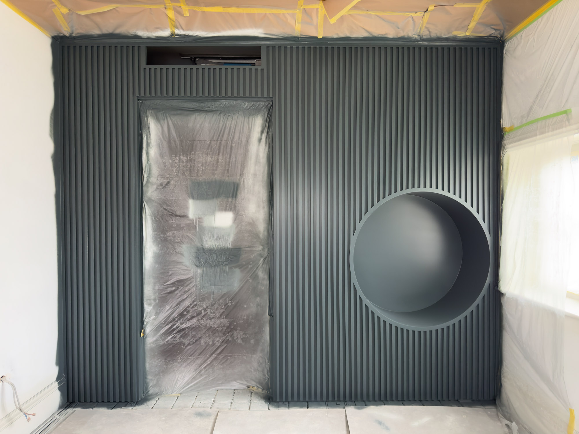 Minimalist living room wall with a beige fireplace, black stove, wall-mounted flat TV, empty built-in shelves, and a light-colored sofa corner.